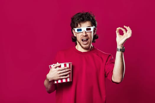 handsome bearded man in 3d-glasses, t-shirt showing popcorn on magenta background