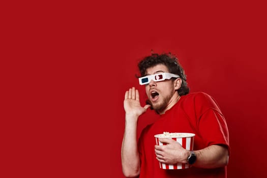 scared handsome bearded man in 3d-glasses holding bucket of popcorn on red background