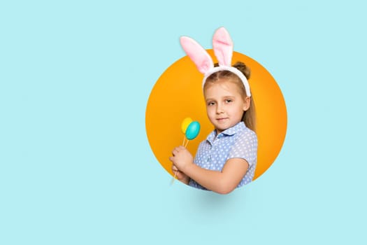 happy little child girl with Easter bunny ears holding colorful eggs on yellow and blue background. Happy easter. space for text