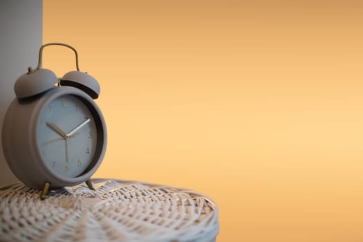 An old analog alarm clock stands on a woven wicker basket and indicates the time. The fuzzy orange light imitates a bedside lamp lit in the evening .
