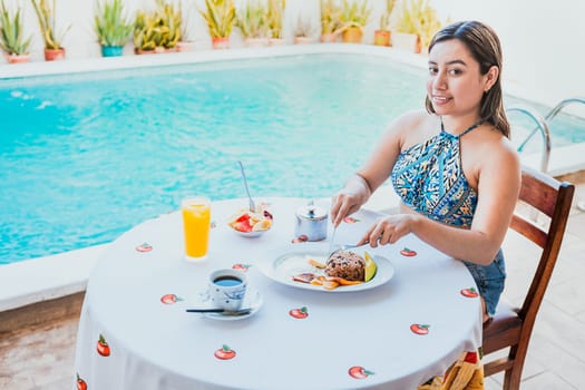 Smiling girl having breakfast near the swim pool. Woman on vacation having breakfast near swimming pool. Breakfast concept near swimming pool