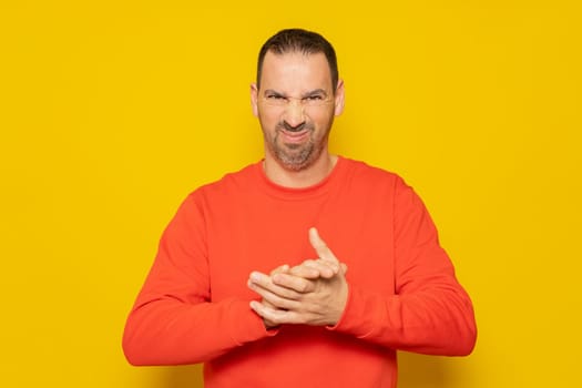 Evil hispanic man rubbing hands on isolated yellow background, person rubbing hands planning some kind of crime