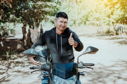 Biker on his motorbike holding safety helmet with thumb up. Concept of Smiling motorcycle cyclist holding safety helmet, Biker man giving thumb up while holding safety helmet