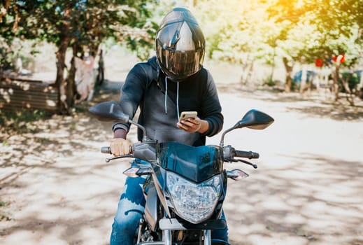 Man on motorbike texting while driving. Motorcyclist on motorcycle using cell phone outdoors. Concept of distracted motorcyclist with cell phone.