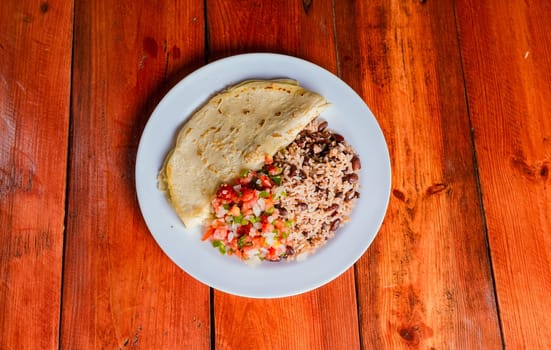 Quesillo dish with gallo pinto and pico de gallo on wooden table. Nicaraguan food Gallo pinto with pico de gallo and Quesillo served