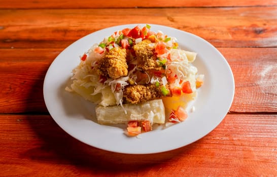 Traditional chicharron dish with cassava and tomato salad. Latin food chicharron con yuca served on wooden table. Nicaraguan dish chicharron with cassava on the table.