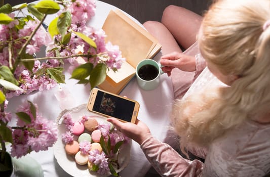 Blonde blogger in a pink dress drinks coffee, reads a book, uses a smartphone, shoots a video for her blog, top view, High quality photo