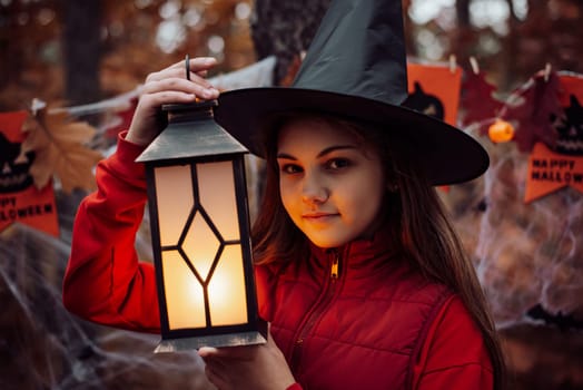 Small girl in witch hat with lantern in dark forest