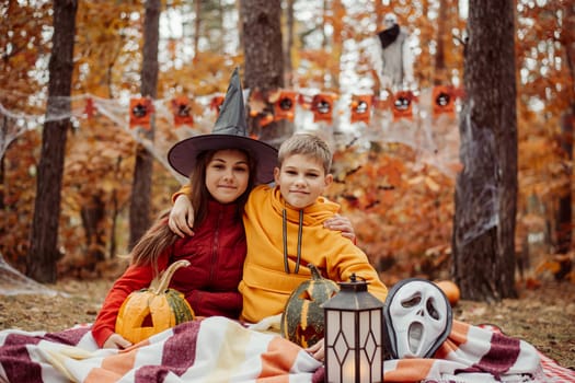 Little boy and girl on picnic pad in forest, halloween decorations around