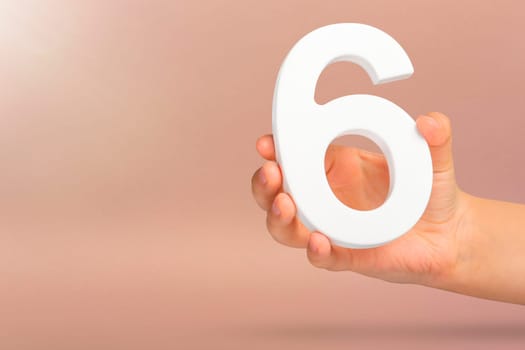 Number six in hand. A hand holds a white number 6 on a red background with copy space. Concept with number six. 6 percent, birthday 6, sixth grade, in sixth grade.