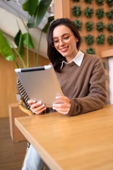 Portrait of happy woman using tablet computer sitting at her desk. Modern technologies and communication. Young female person studying or working online on touch pad looking at screen device. Vertical