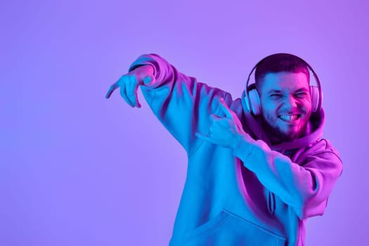 handsome man listening to music with wireless headphones on purple neon background. Neon lighting