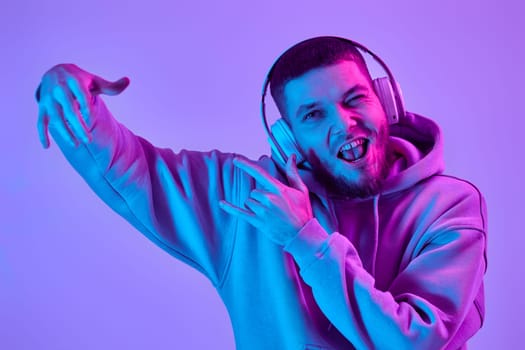 handsome bearded man with headphones in sweatshirt enjoying favorite music on purple neon background. Neon lighting