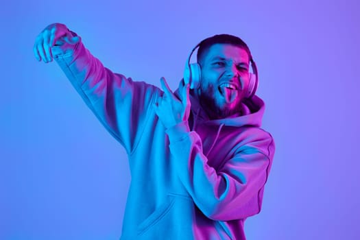 handsome man listening to music with wireless headphones on purple neon background. Neon lighting