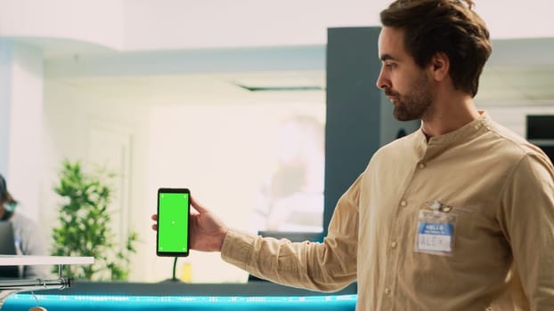 Man worker holding smartphone with greenscreen, showing blank copyspace template on mobile phone. Caucasian market assistant using isolated chroma key display in clothing store.