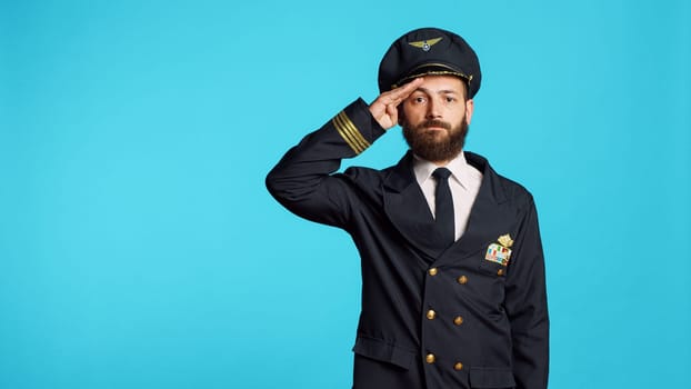 Young pilot showing military salute in studio, expressing respect for army. Plane captain serving flying industry as airliner, working on commercial flights and aerial transportation.