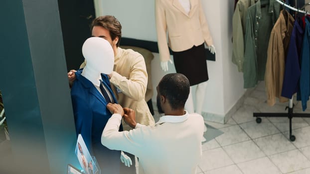 Group of customers looking at new fashion collection in clothing store, diverse people checking boutique merchandise in shopping center. Men and women visiting retail shop. Handheld shot.