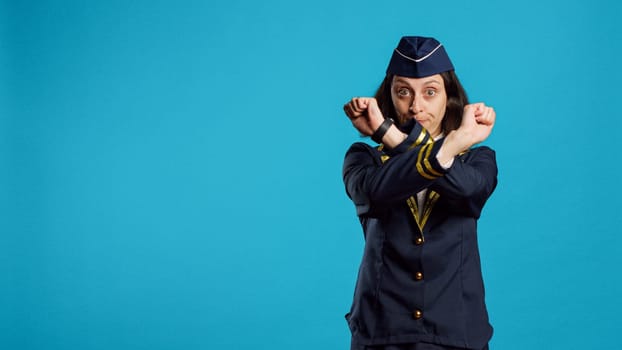 Young air hostess doing x shape gesture and showing disapproval, saying no with rejection or denial symbol with hands. Female airliner expressing disagreement and refusal sign.