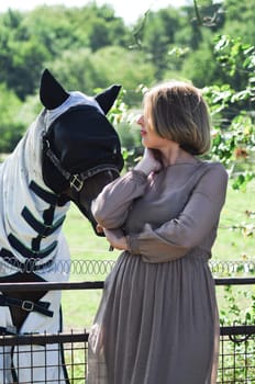 confident blonde woman feeding a horse among tall trees in summer,the countryside, rural, rustic scene, High quality photo