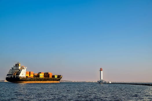 A container ship leaves the port near the lighthouse. Evening. High quality photo