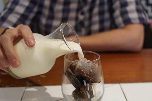 Milk Being Poured Into Glass Iced Coffee on the table in a cafe.
