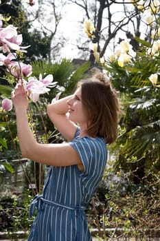 blonde with pleasure inhales an aroman of magnolia flowers standing under a tree. High quality photo