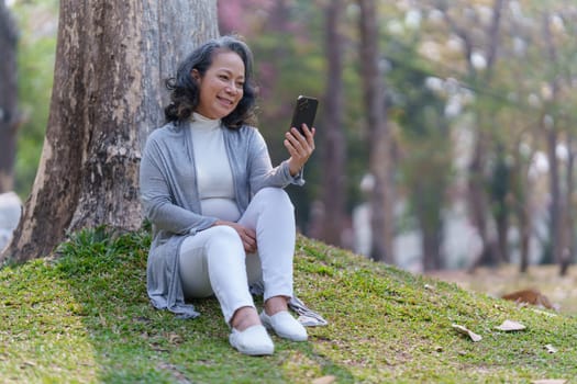 Cheerful overjoyed woman happy and enjoying peaceful beautiful in park and using social media by smartphone.