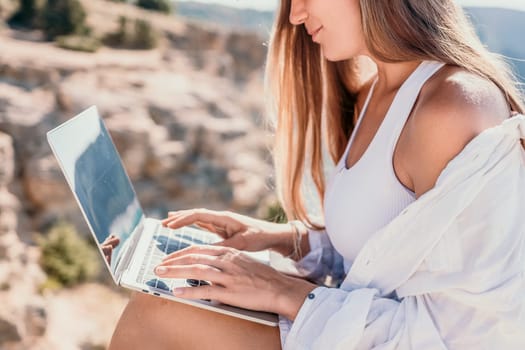 Digital nomad, Business woman working on laptop by the sea. Pretty lady typing on computer by the sea at sunset, makes a business transaction online from a distance. Freelance remote work on vacation