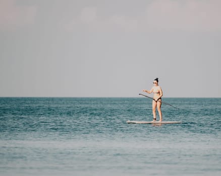 Sea woman sup. Silhouette of happy middle aged woman in rainbow bikini, surfing on SUP board, confident paddling through water surface. Idyllic sunset. Active lifestyle at sea or river