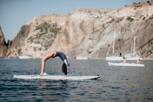 Woman sup yoga. Middle age sporty woman practising yoga pilates on paddle sup surfboard. Female stretching doing workout on sea water. Modern individual hipster outdoor summer sport activity