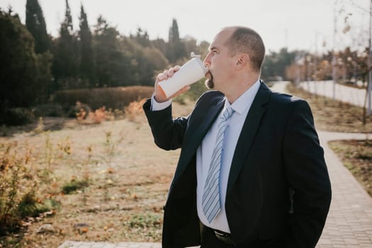 Mature entrepreneur drink coffee in autumn park. Senior executive rest in city park.