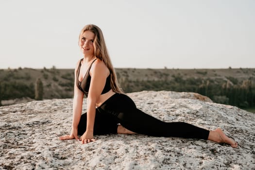 Well looking middle aged woman with long hair, fitness instructor in leggings and tops doing stretching and pilates on the rock near forest. Female fitness yoga routine concept. Healthy lifestyle.