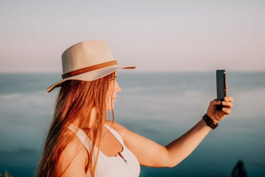 Woman travel sea. Happy tourist in hat enjoy taking picture outdoors for memories. Woman traveler posing on the beach at sea surrounded by volcanic mountains, sharing travel adventure journey