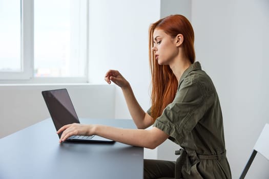 woman interested in work sits at a table and works in a laptop in a bright room. High quality photo
