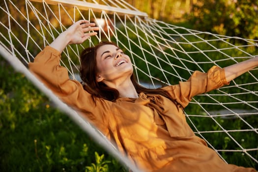 a happy woman is resting in a hammock with her eyes closed and her hands behind her head smiling happily enjoying the day. High quality photo