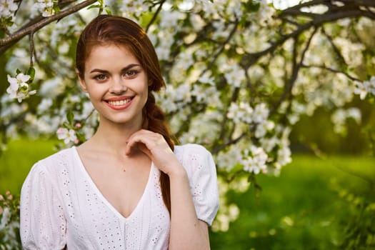 a joyful, carefree woman in a light dress stands against the background of a flowering tree. High quality photo