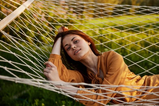 a happy woman is resting in a mesh hammock, resting her head on her hand, smiling happily looking at the camera, enjoying a sunny day. High quality photo