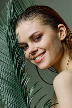 a refined, elegant woman stands with a green palm leaf holding it near her face, smiling pleasantly. Vertical photo without retouching. High quality photo