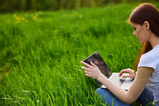 a woman sits at work in a laptop being outdoors in a field. High quality photo