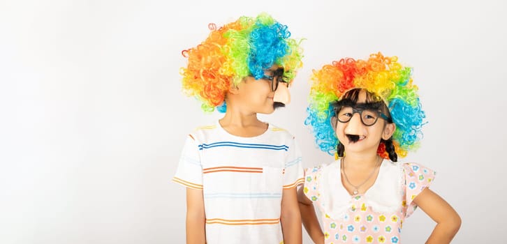 April Fool's Day. Two brothers funny kid boy and little girl clown wears curly wig colorful big nos and glasses and has mustache isolated on white background, Happy children festive decor