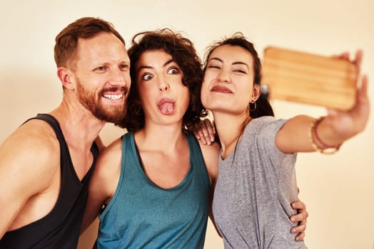 Having fun takes the work out of workout. a group of young men and women taking selfies in yoga class