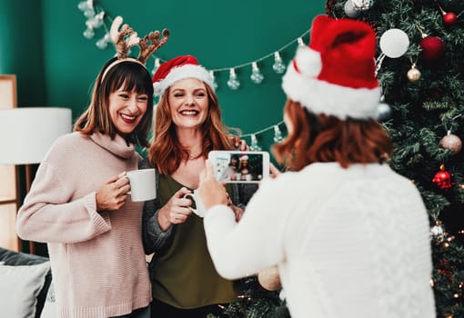 Stay just like that. of a cheerful middle aged woman taking a picture of her two friends at home during Christmas time