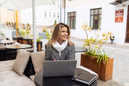 young european woman model in street cafe with laptop in spring.