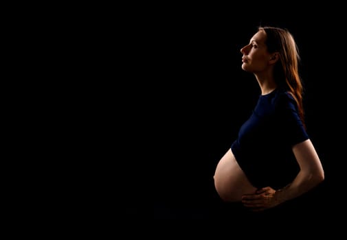 Beautiful pregnant woman over black background. Artistic low key light in studio. High quality photo