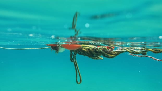 Underwater photo - red buoy and tangled ropes near sea surface. Abstract marine background.