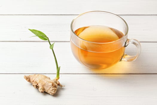 Cup of freshly brewed amber tea, glass wet from steam, dry ginger root with green sprout next to it.