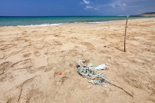 Perfect empty unspoiled beach, small pile of rubbish (tangled plastic ropes) on fine sand, calm sea in background. Ocean littering concept. Karpass, Northern Cyprus