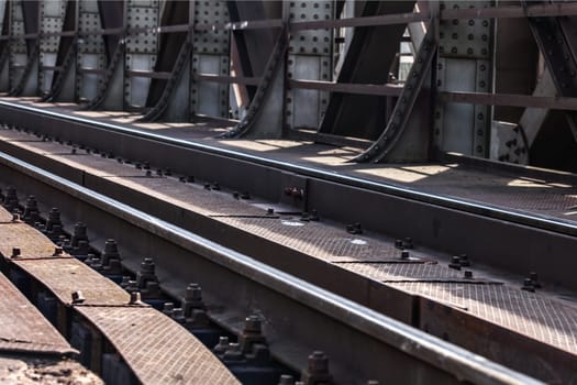 Detail on railway tracks at steel rail bridge lit by sun.