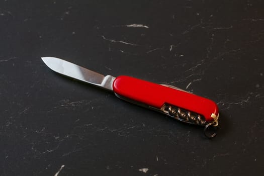 Red pocket knife on black table.