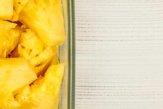 Tabletop view, detail - yellow pineapple cut in pieces, in square glass bowl, white boards desk / space for text on right.